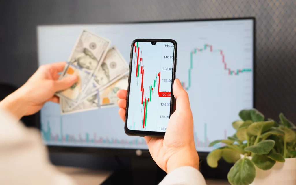 mobile copy trading app showing trading signals in front of a monitor screen