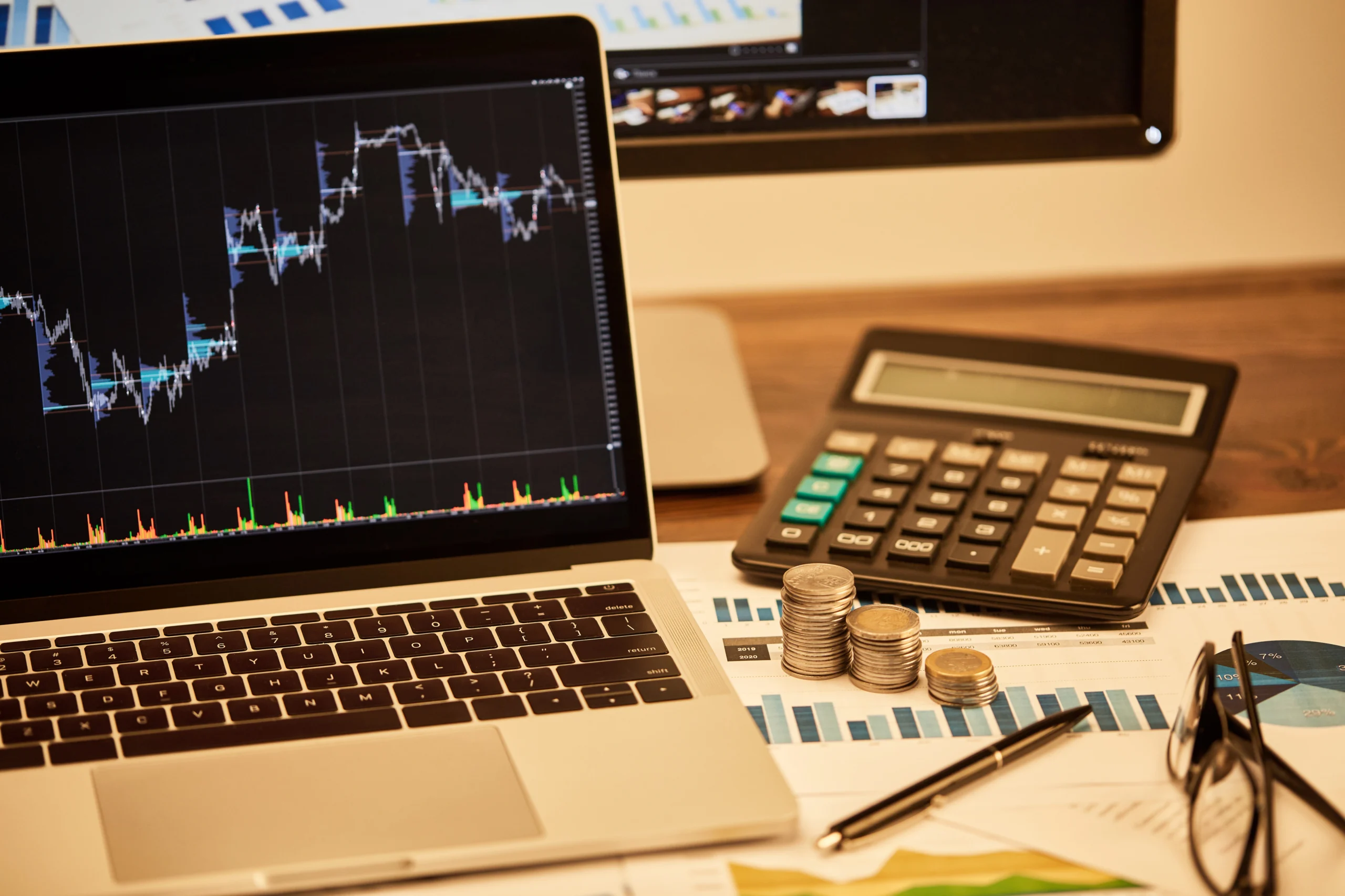 trading chart on a laptop with calculator and stacks of coins beside it