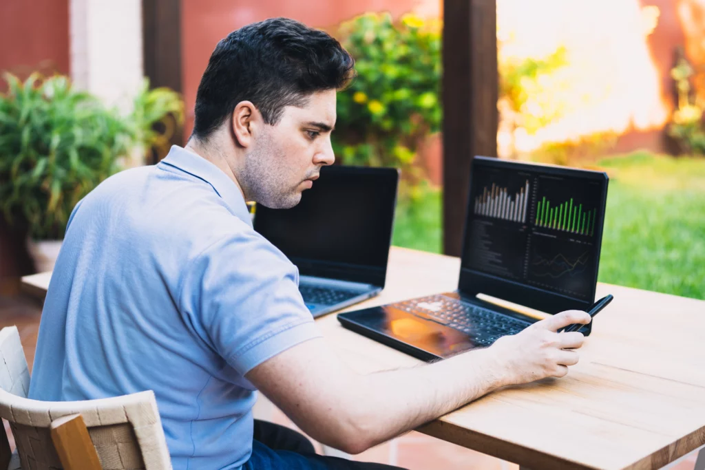 trader looking at mobile phone with trading chart on laptop