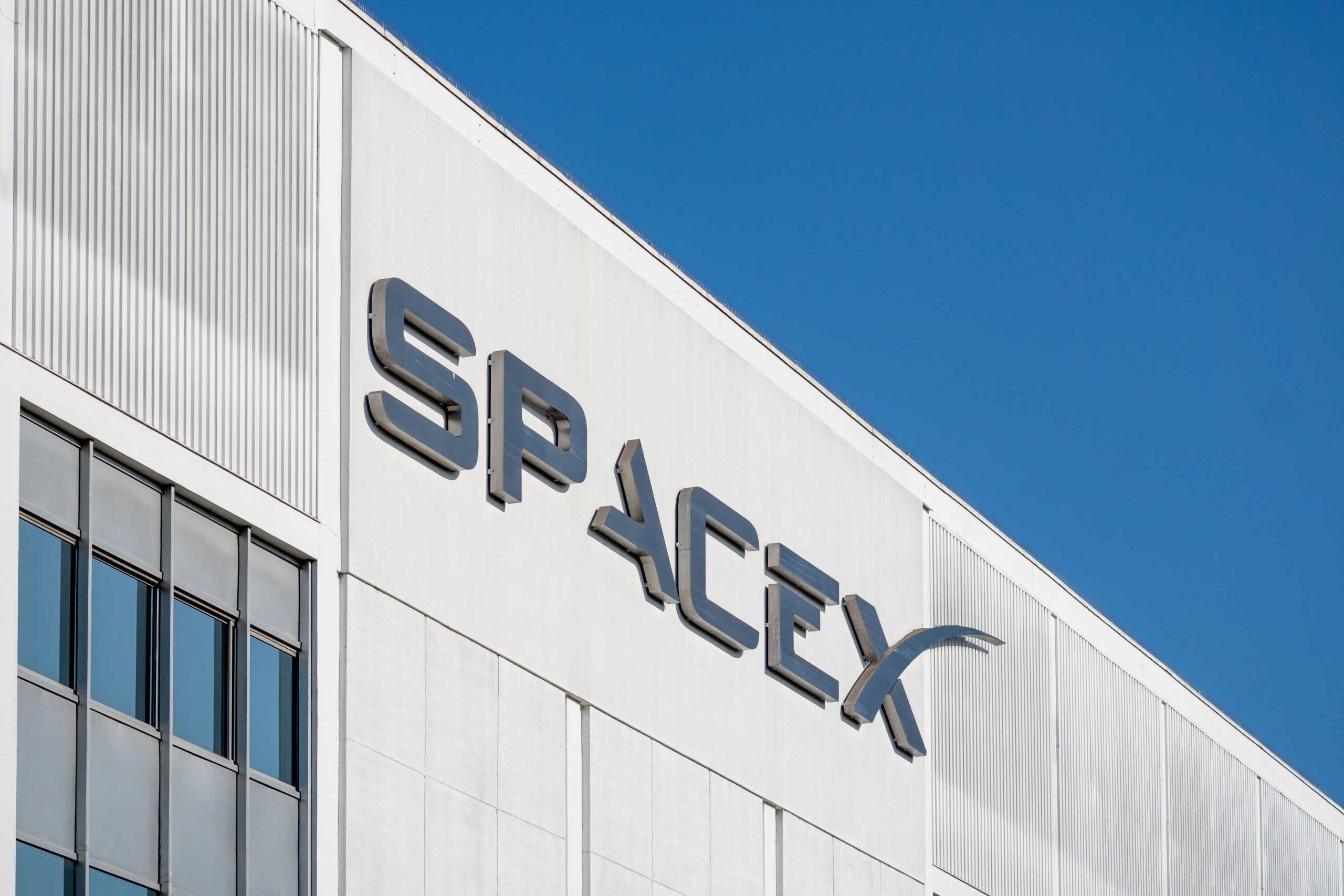 White modern office building facade with large glass windows and blue sky, featuring raised signage on the wall.