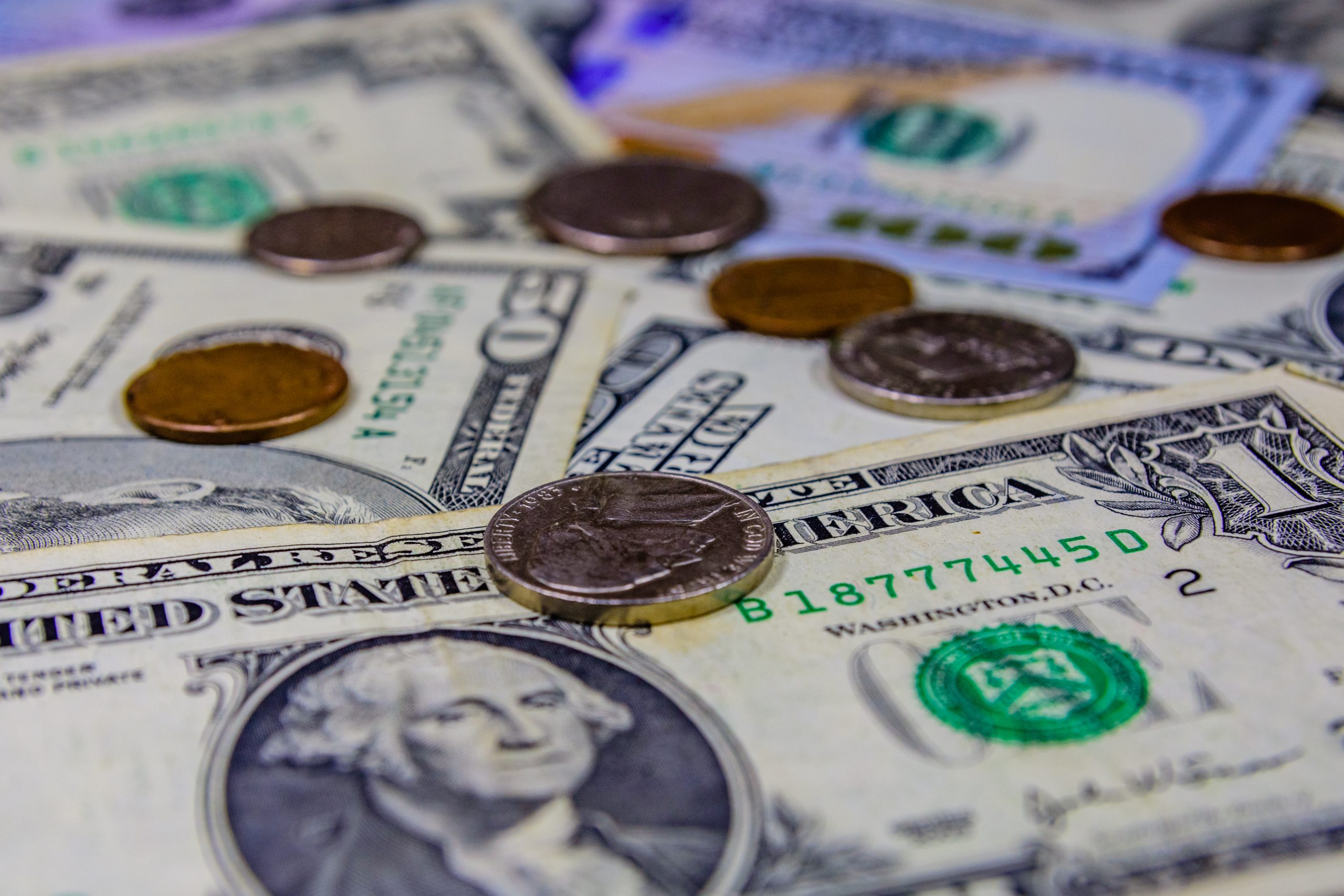 Close-up of scattered US currency: pennies and other coins atop overlapping dollar bills (including $1, $5, and $10 notes).