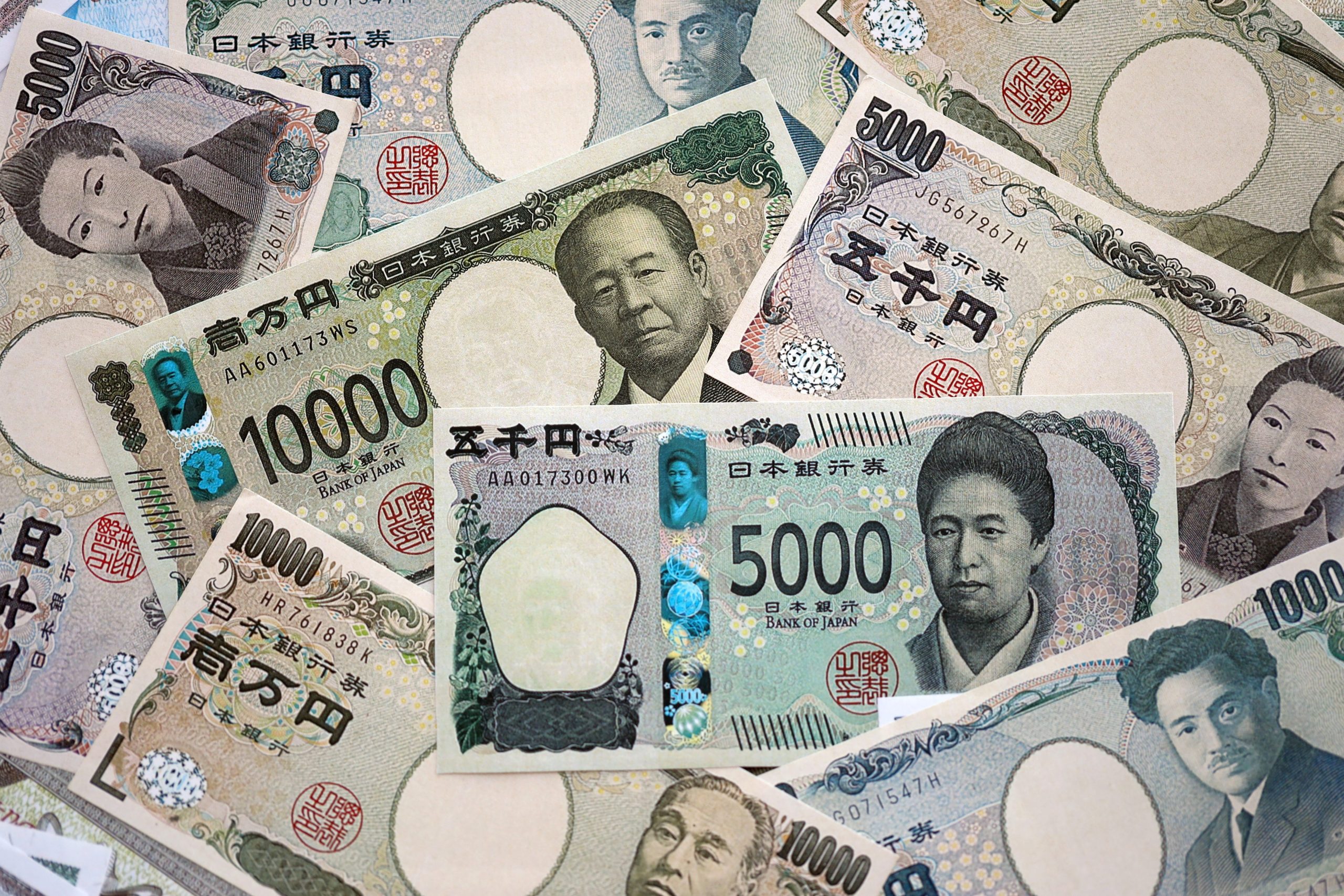 Several Japanese yen banknotes overlapped, displaying portraits and ornate patterns (1000, 5000, 10000 yen).