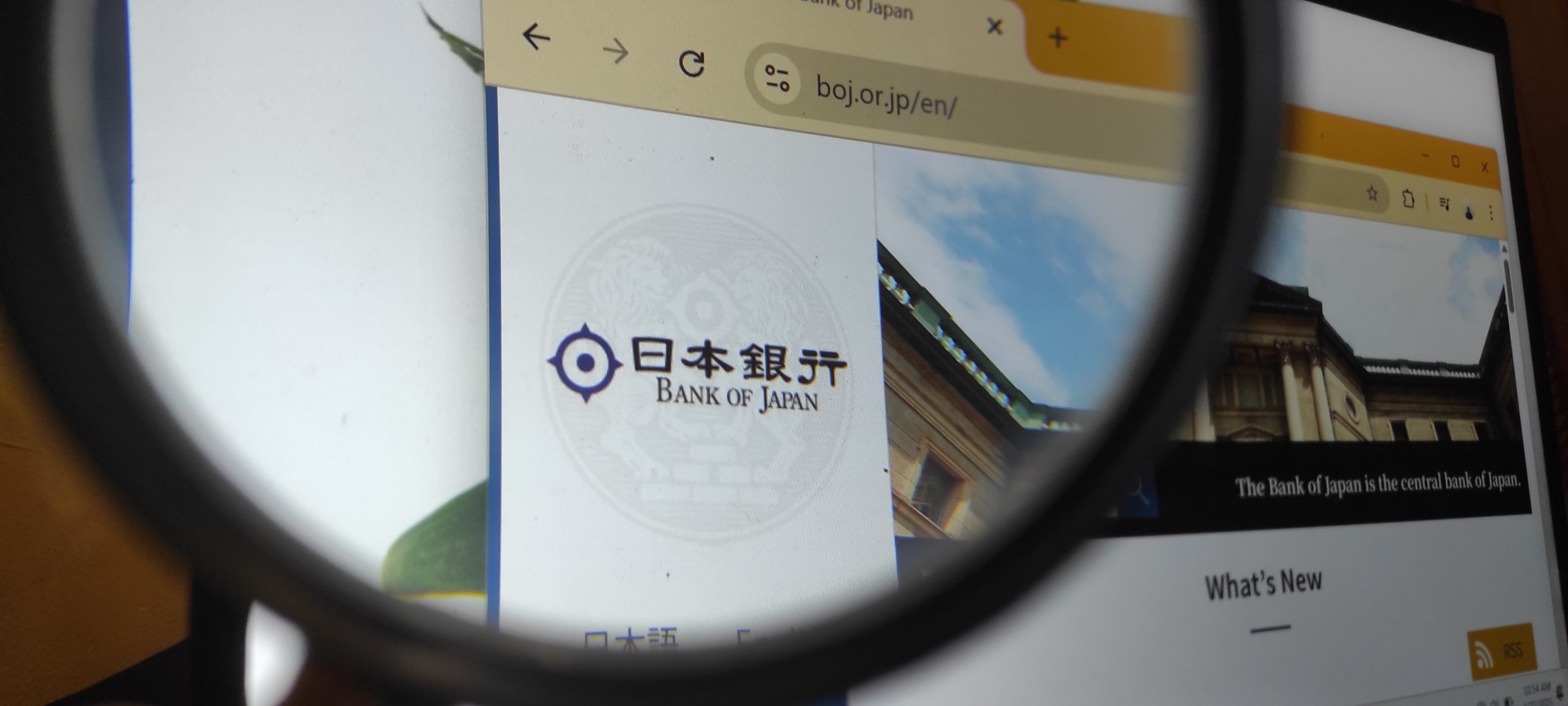 Screen showing Bank of Japan logo and text in a browser, viewed through a magnifying glass.