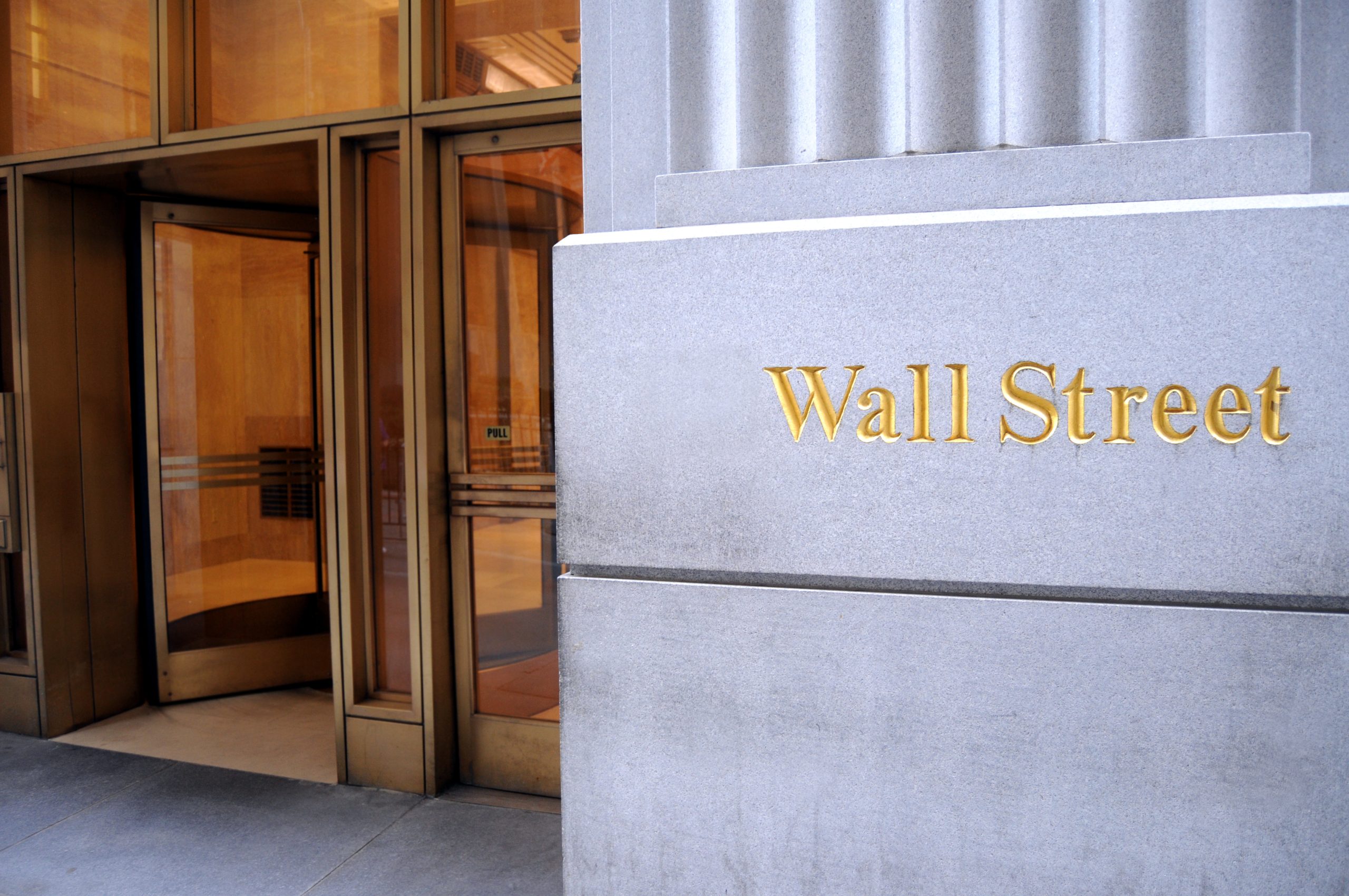 Stone gray facade with a gold 'Wall Street' sign beside a glass entrance on the left.