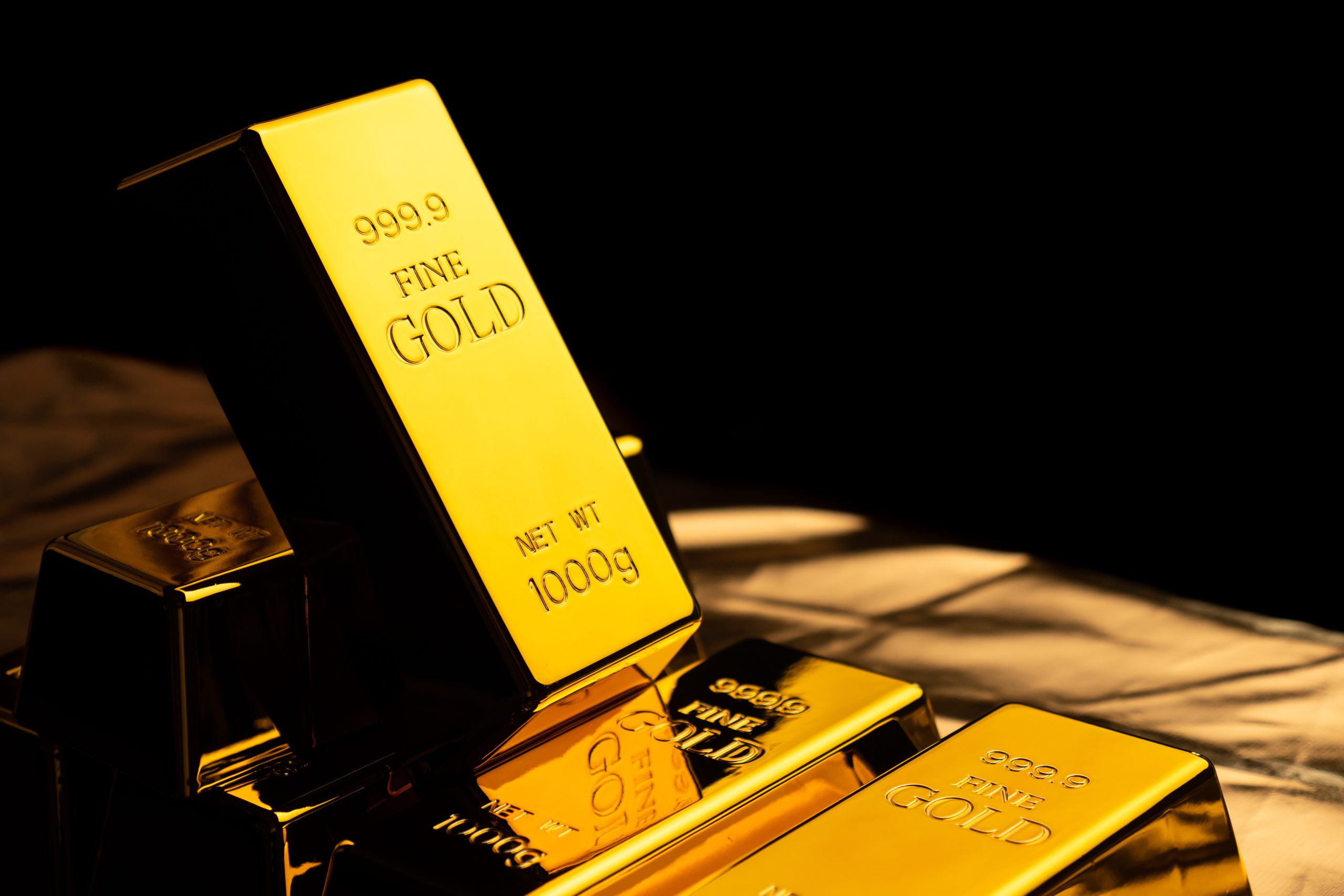 Stack of shiny gold bars on a reflective surface with a warm glow, stamped 999.9 FINE GOLD and 1000 g.