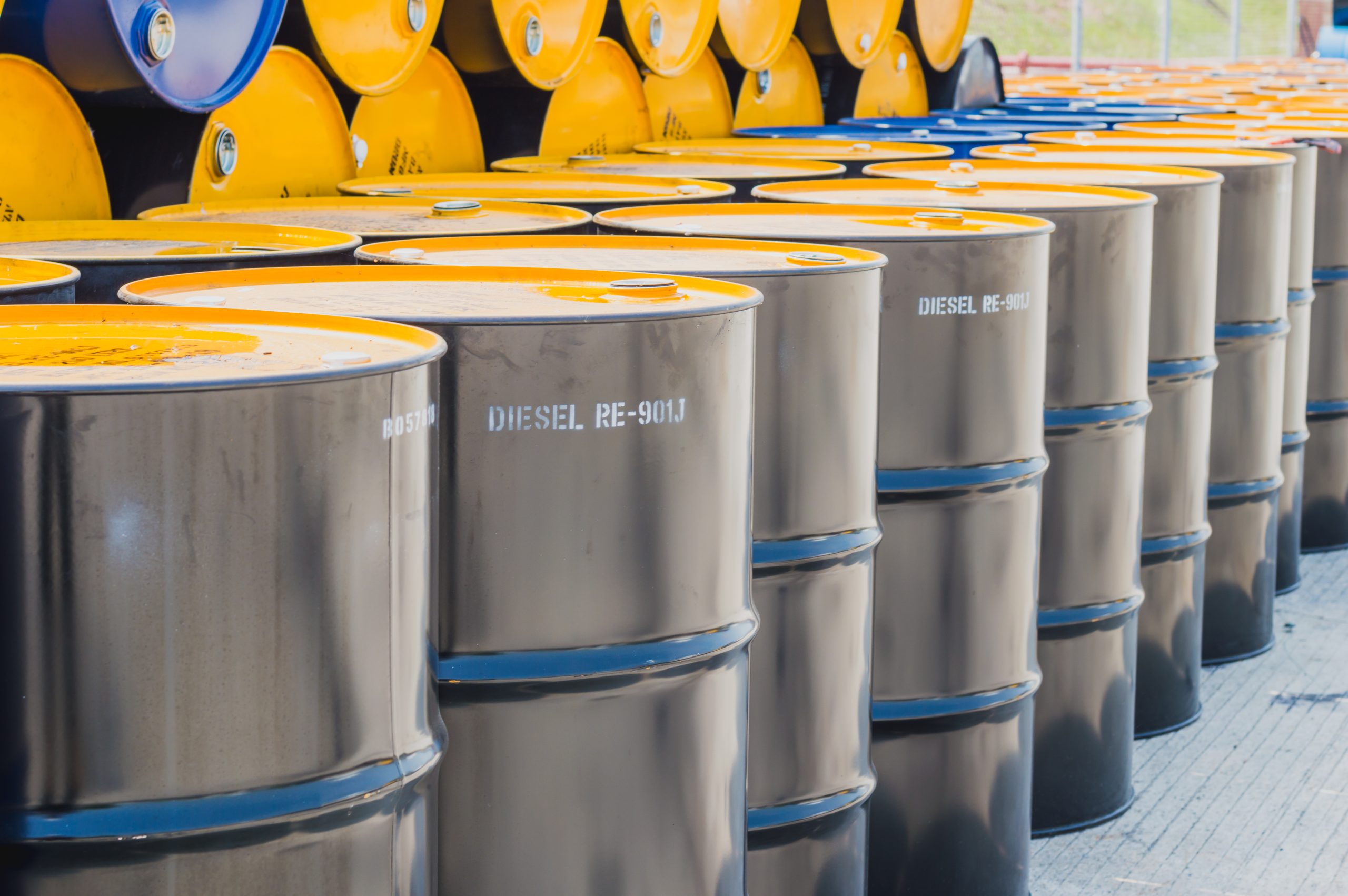 Row of gray diesel drums with yellow tops lined up in an outdoor storage yard.
