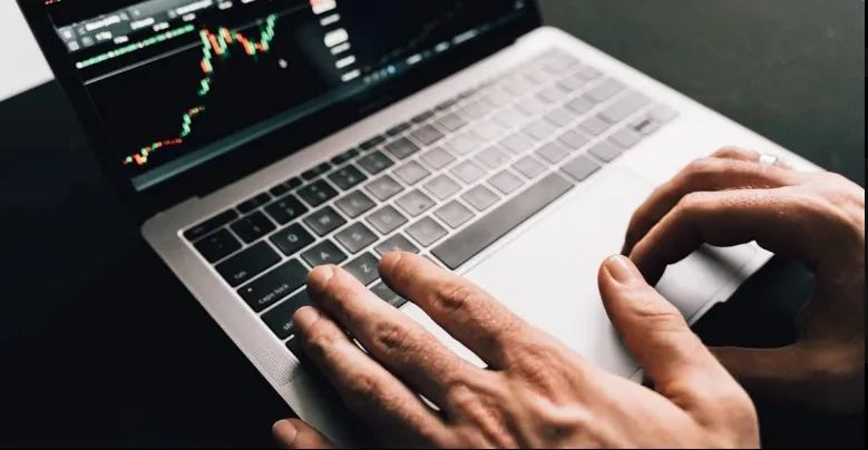 Hands operating a laptop displaying candlestick trading charts.