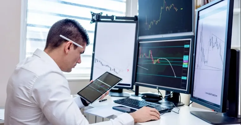 Trader reviewing forex charts on several monitors and a tablet.