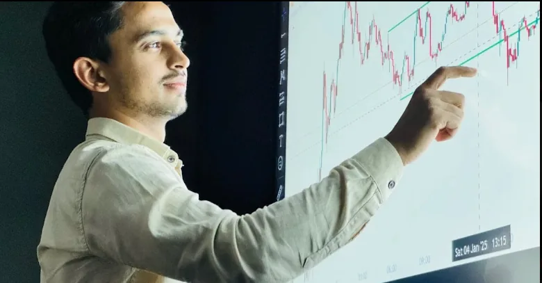 Man pointing to a candlestick chart on a large screen.